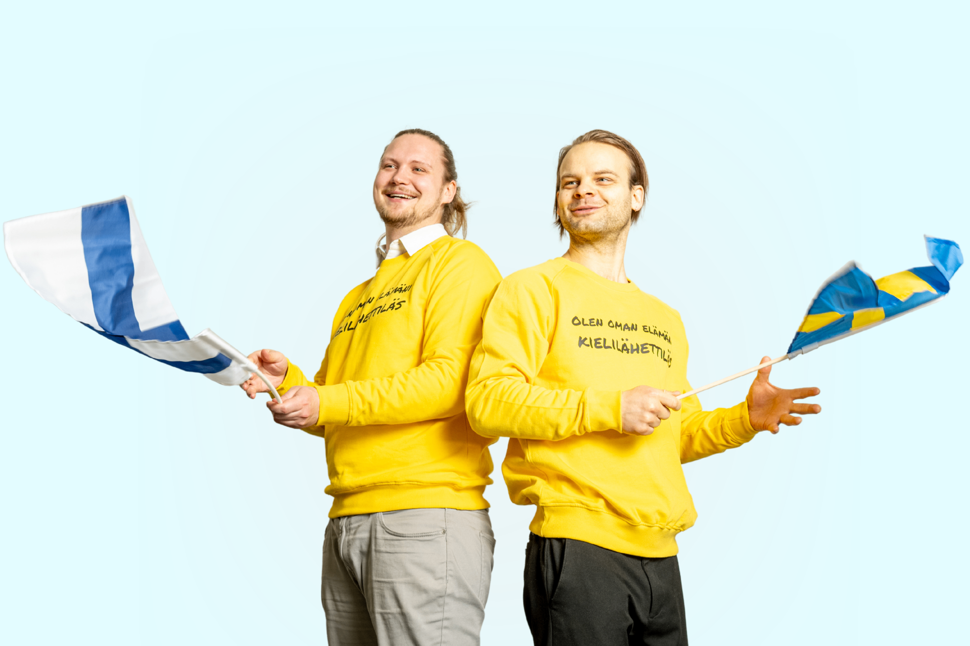 Två personer i gula tröjor som håller finsk och svensk flagga